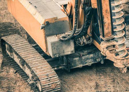 Construction drill rig with tracks; yellow and black, on dirt.