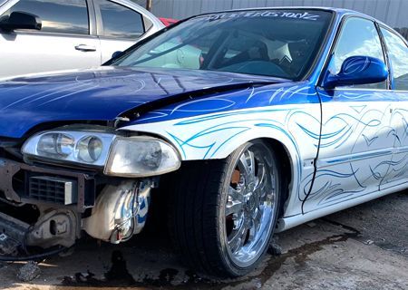 Blue and white car with custom paint, chrome wheels, and missing front bumper.