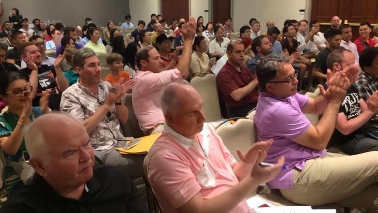 A large group of people are sitting in a room clapping their hands