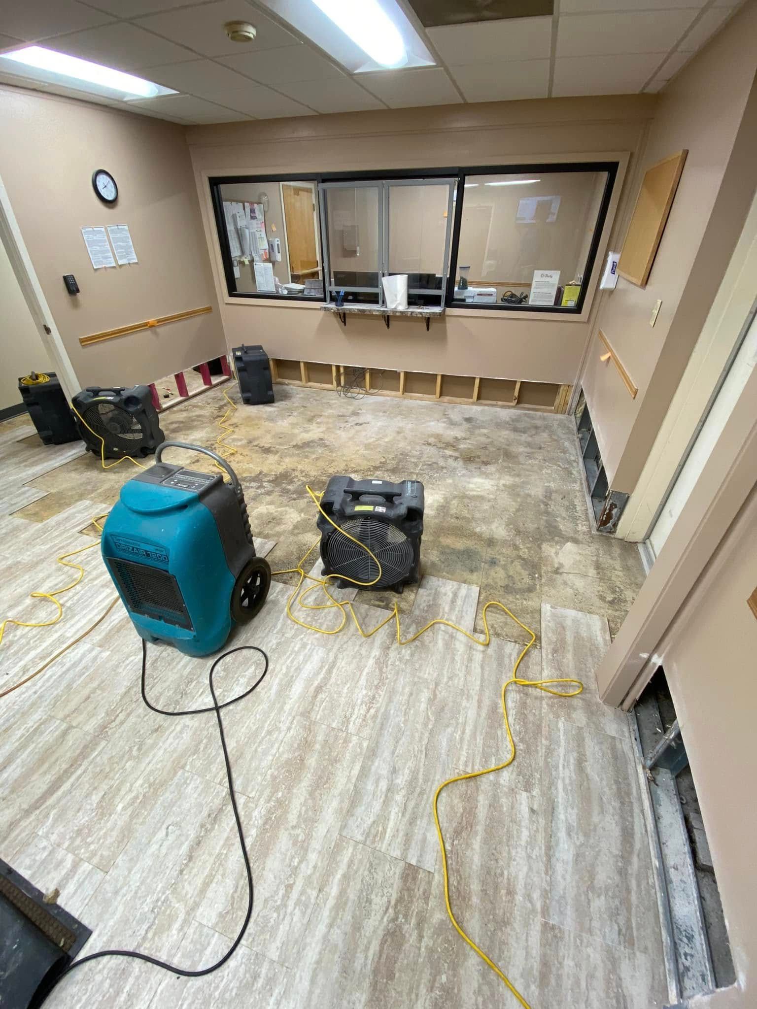 Office under renovation with protective floor covering, a teal chair, and construction materials near a service window.