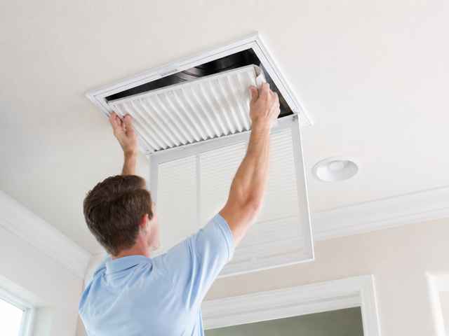 Man installing or replacing a ceiling air filter in a white vent opening