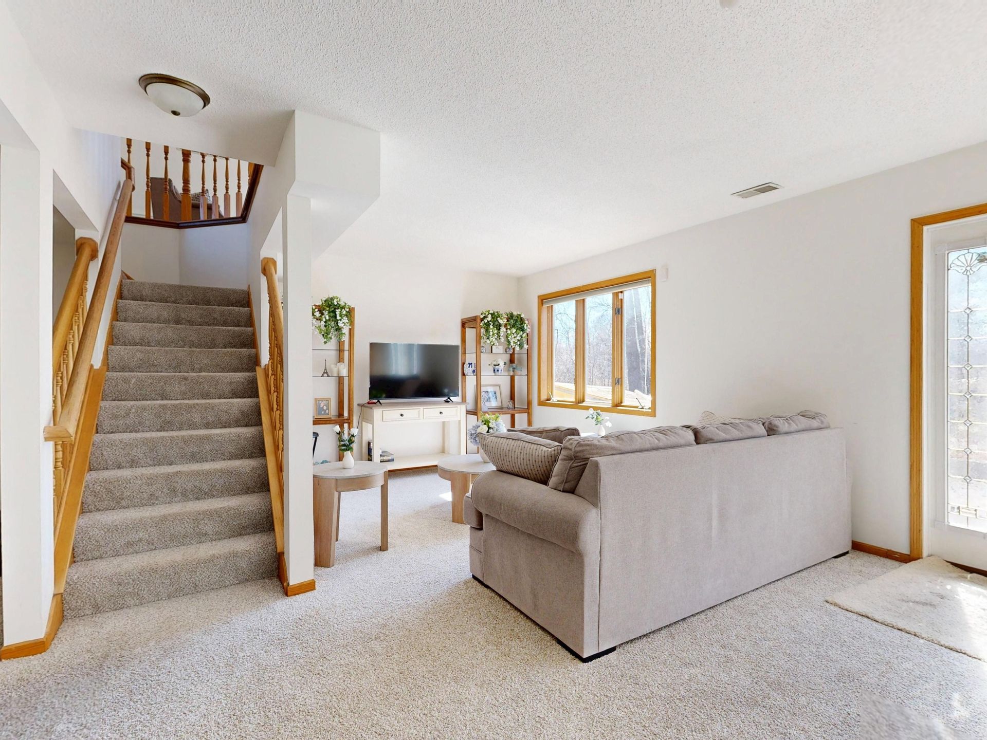 Carpeted living room with a gray sectional, TV, and staircase with wooden railing