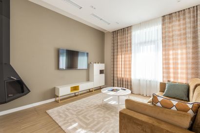 Bright modern living room with tan sofa, wall-mounted TV, white console, and large sunlit windows
