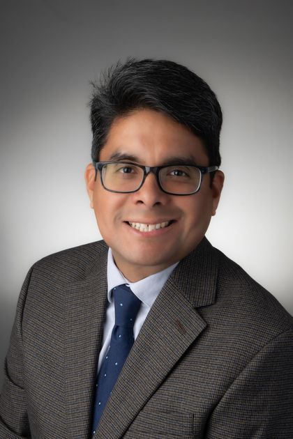 A man wearing glasses and a tie is standing with his arms crossed.