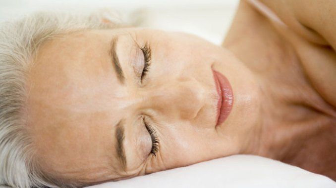 An older woman is sleeping on a bed with her eyes closed.