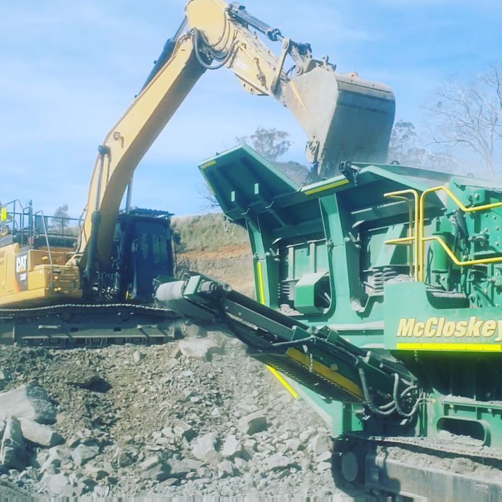 Yellow excavator loading rocks into a green McCloskey rock crusher — Auto Watt in Kelso, NSW