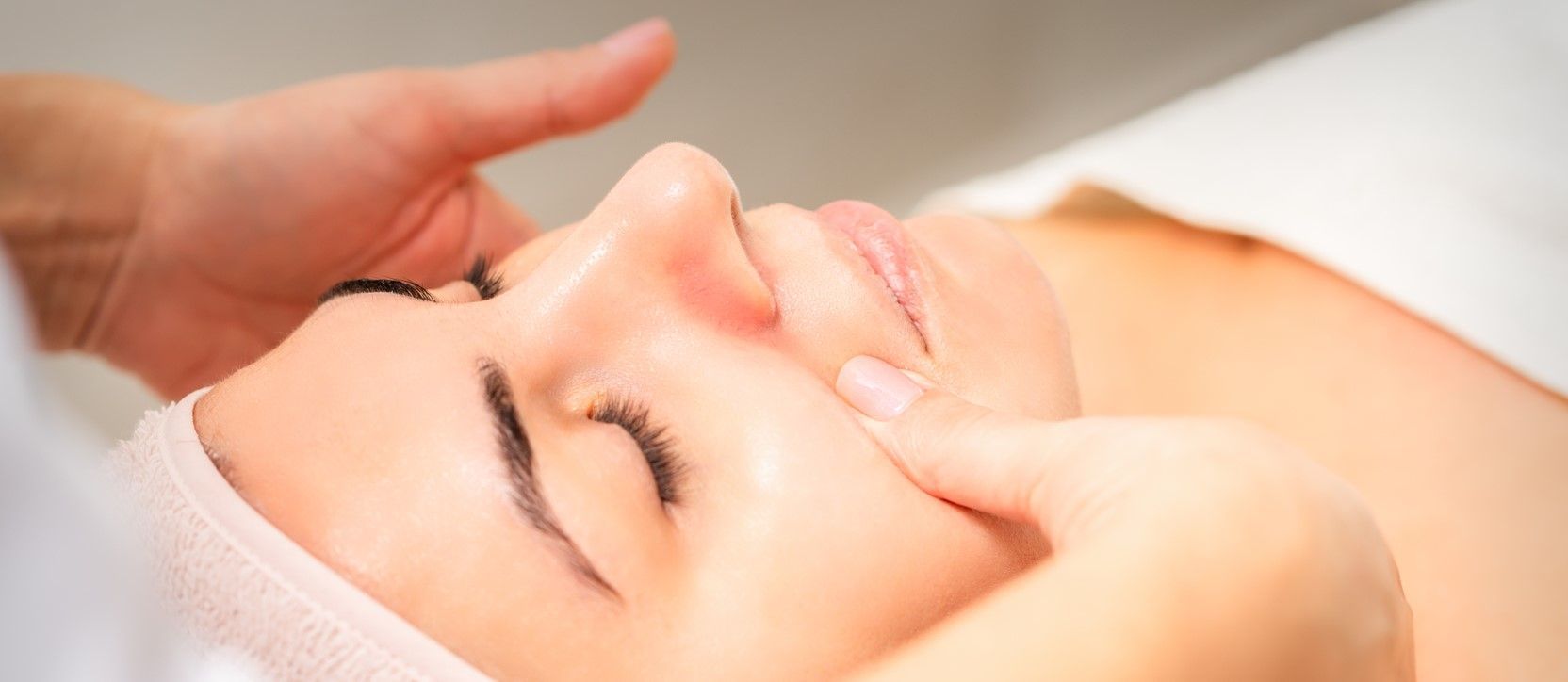 Person receiving facial massage. Face is close up, hands on the face. Eyes are closed.