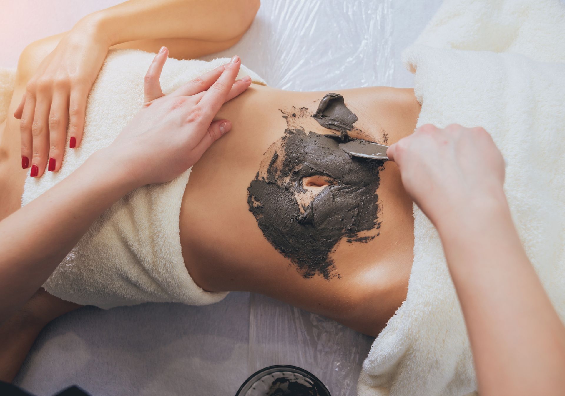 Person receiving a mud treatment on their abdomen in a spa setting, hands applying the mud.