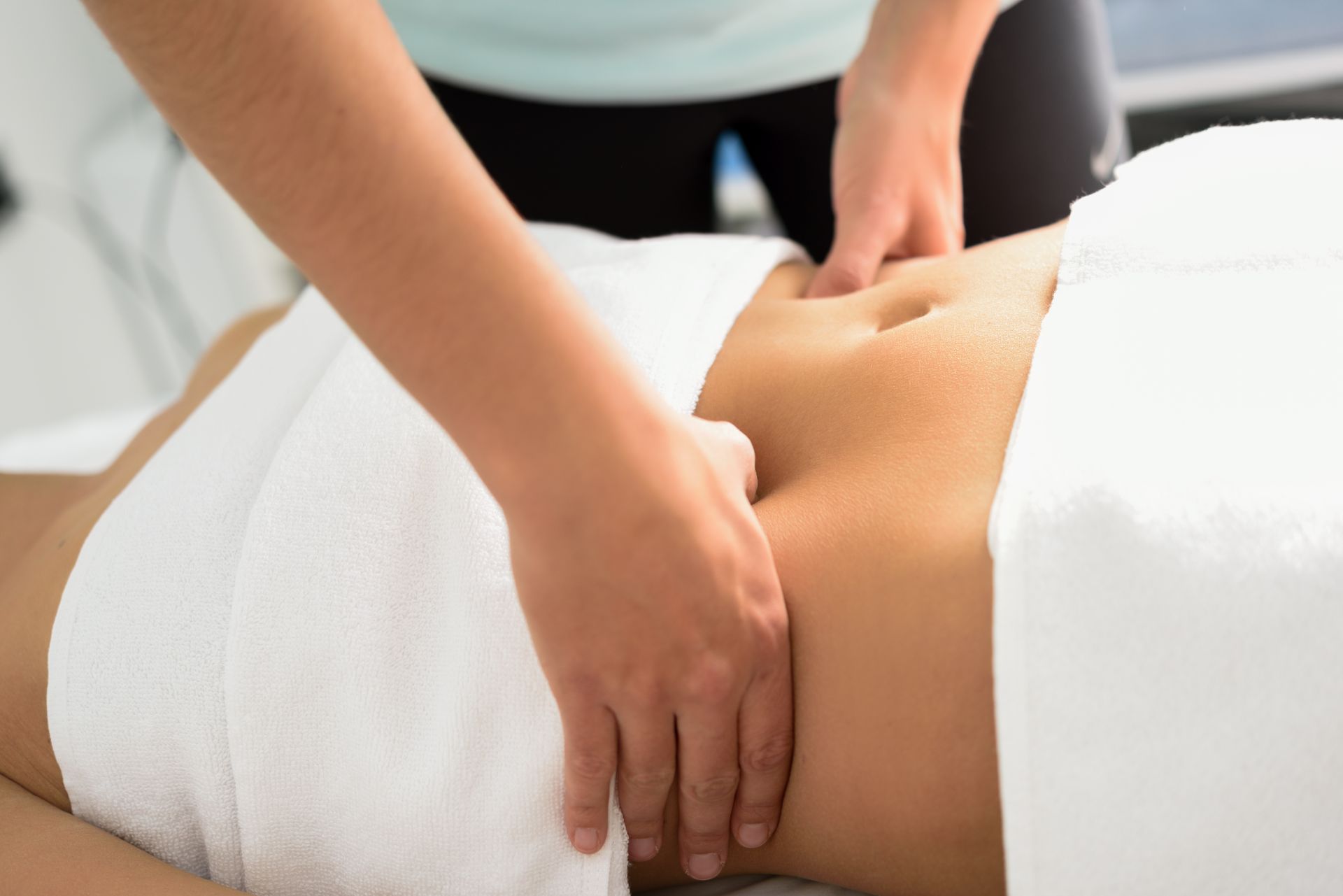 Hands massaging a person's abdomen, partially covered with a white towel, in a health setting.