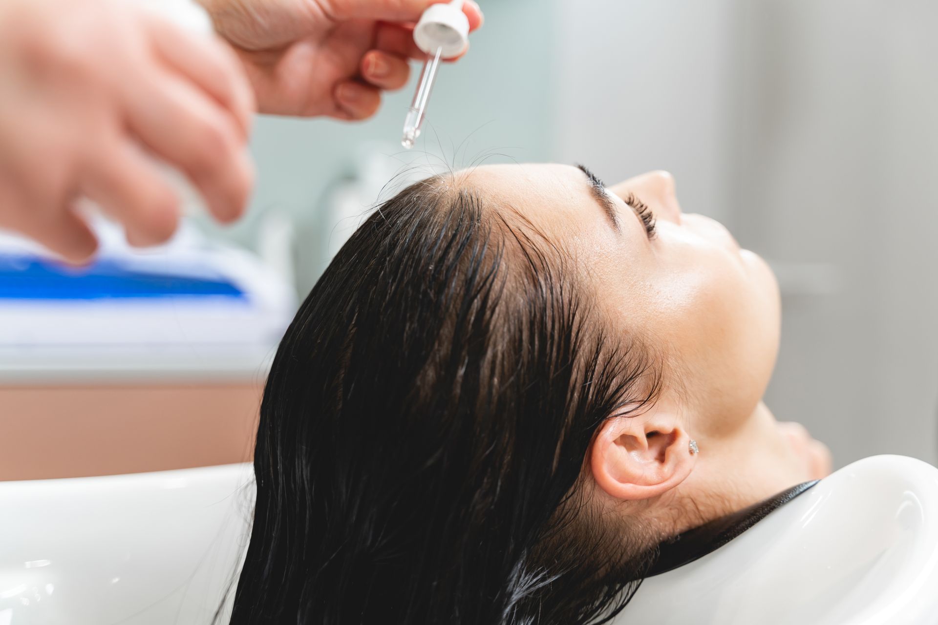 Person having hair oil applied to their scalp in a salon setting.