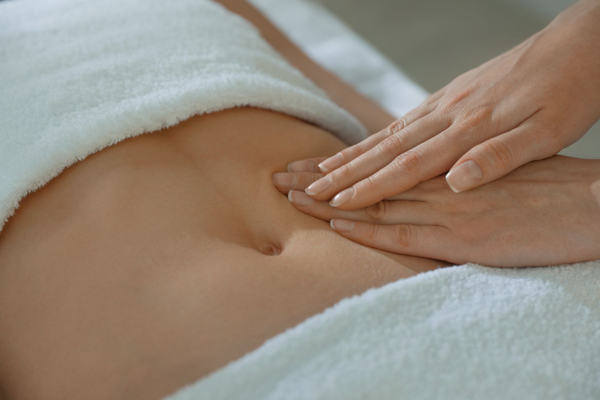Hands massaging a person's abdomen, on a white towel.
