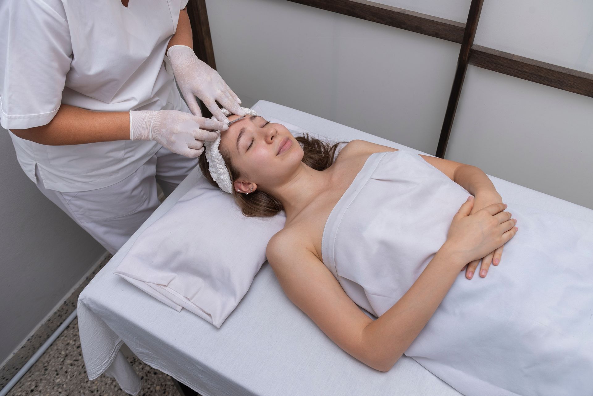 Person receiving facial treatment at a spa; esthetician's hands gloved.