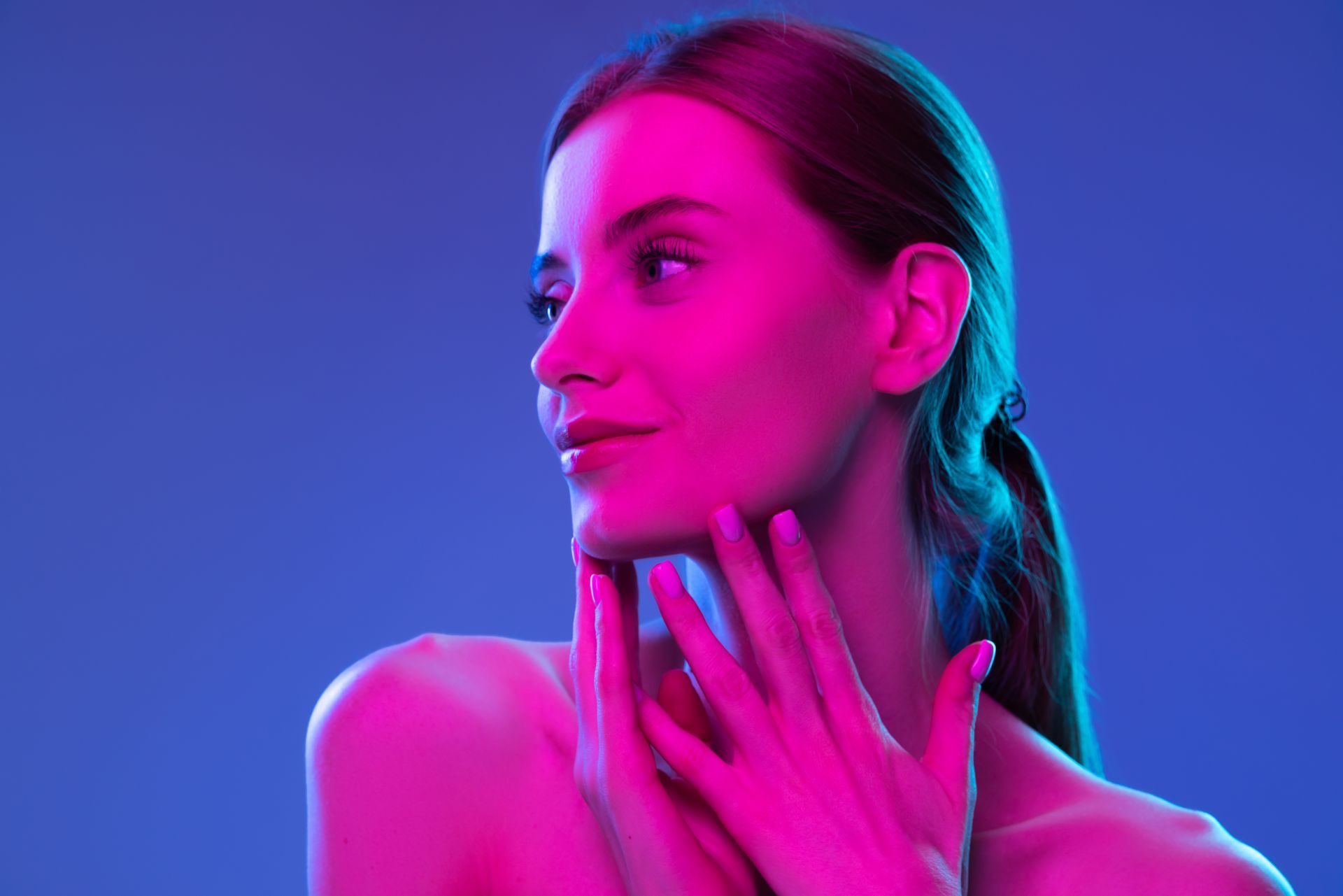 Woman with hands near her face, lit with pink and blue neon lights.
