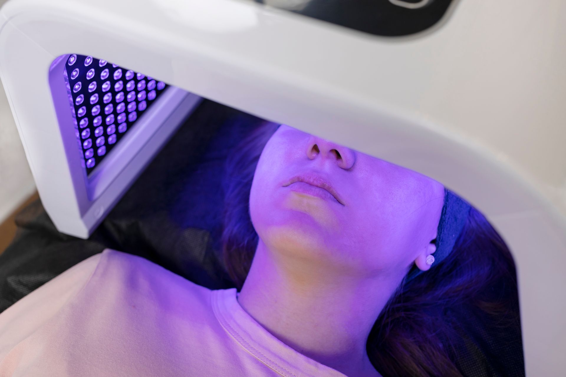 Person undergoing LED light therapy; lying down with purple light on face.