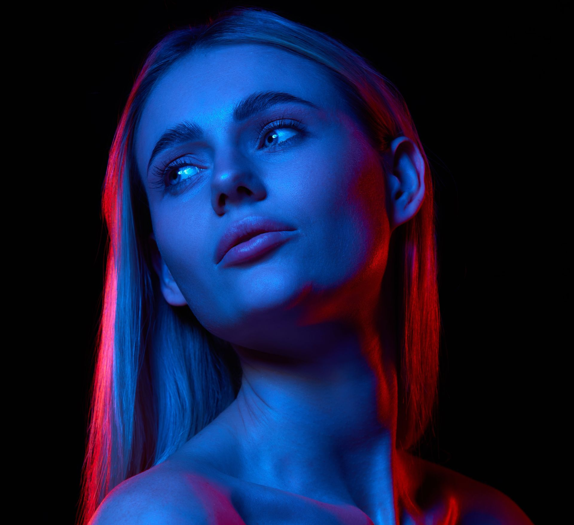 Woman in blue and red lighting, looking upwards, against a black background.