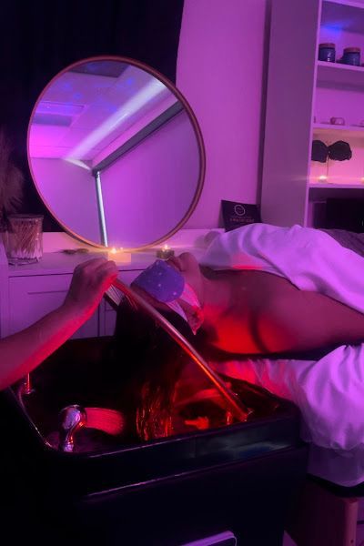 Person receiving a spa treatment. Hair is washed in a basin under red light. A person holds a nozzle over the hair.