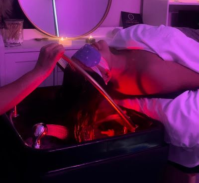 Person receiving a hair treatment at a salon, face up. Hair is in a basin, lit with red light.