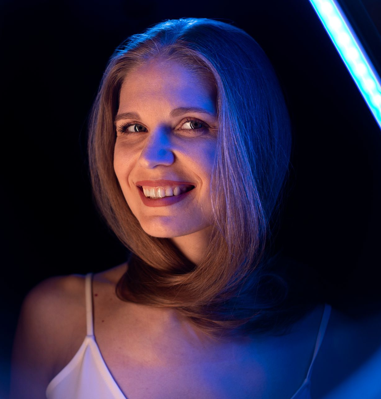Woman smiling, lit by blue neon light against black background.