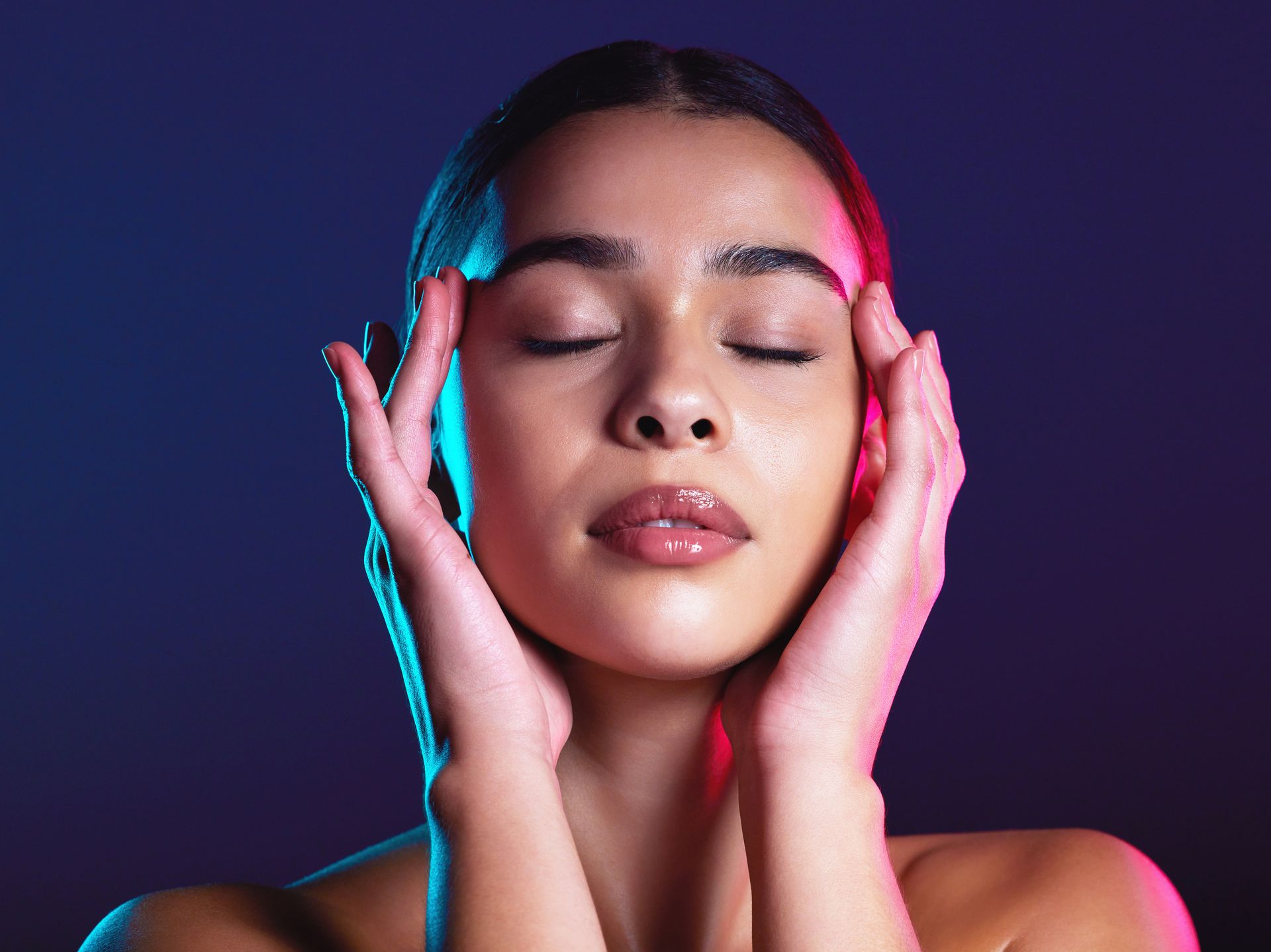 Woman with closed eyes, hands on temples; blue and red light illuminates the face and background.