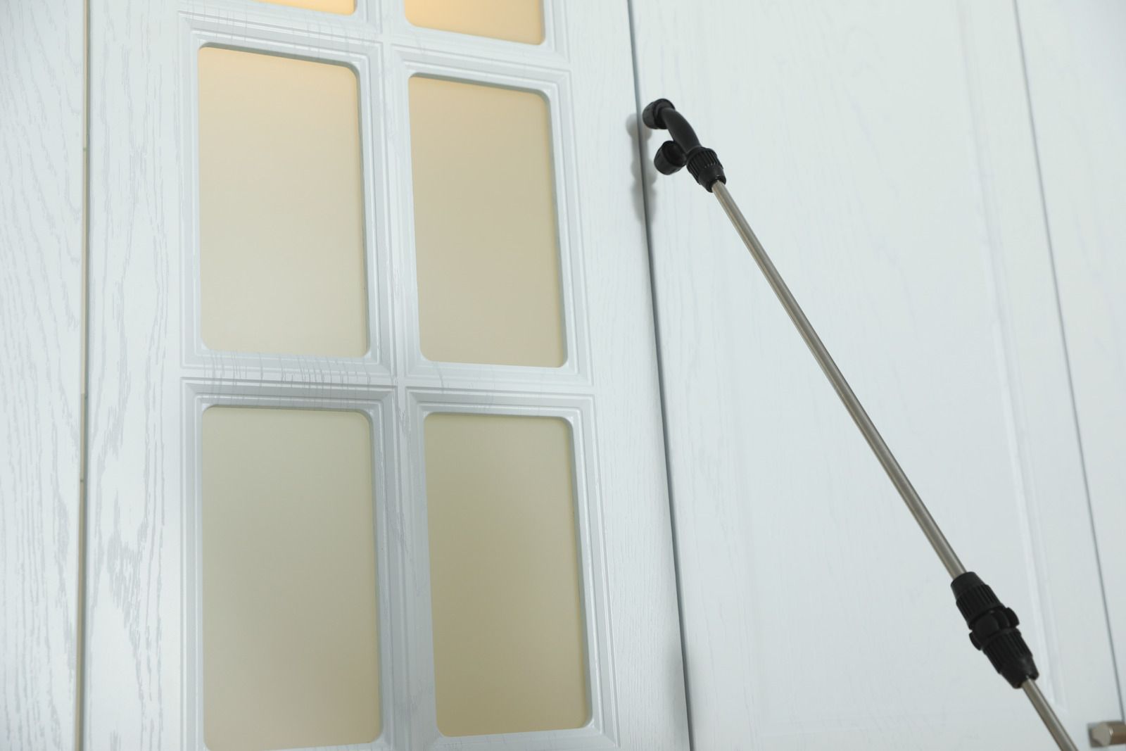 A close-up of a sprayer nozzle applying liquid treatment to the edge of a white paneled door.