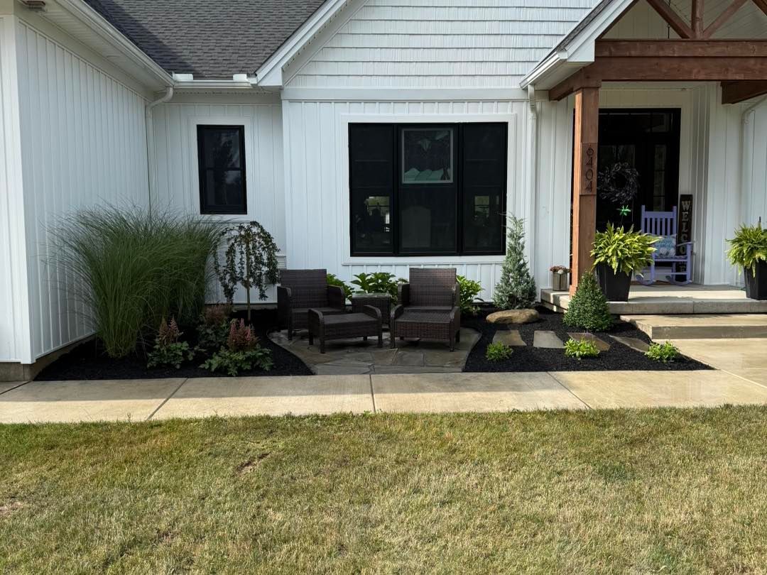 White house exterior with dark trim and patio seating. Landscaping includes plants and mulch.