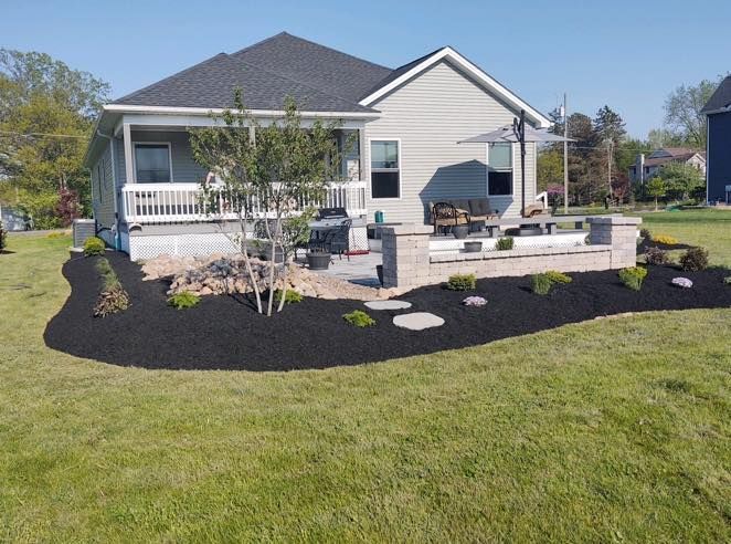 Backyard patio with landscaping, house with gray siding, black mulch, green grass.