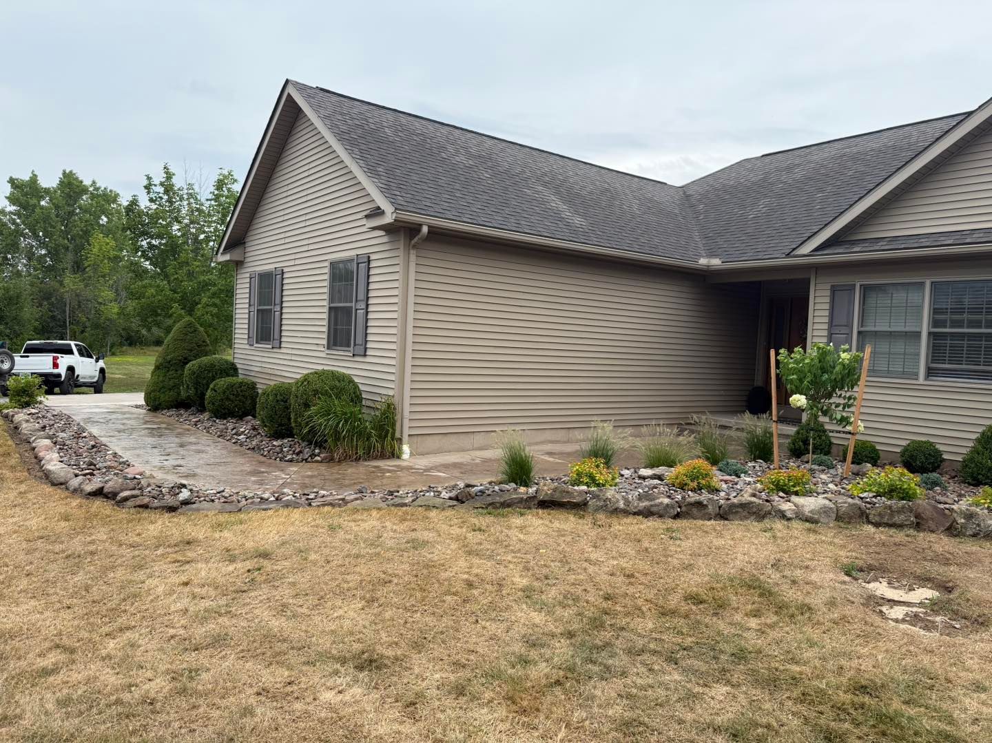 Tan house with gray roof, landscaping with rocks, bushes, and dry grass in the front yard.