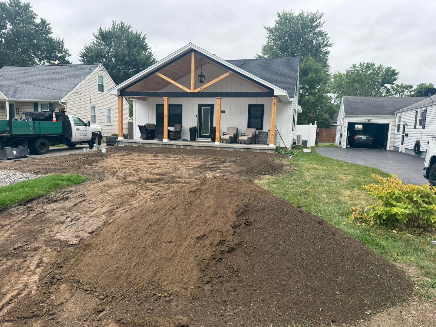 A white house with a porch and construction in progress. A pile of dirt in the front yard.