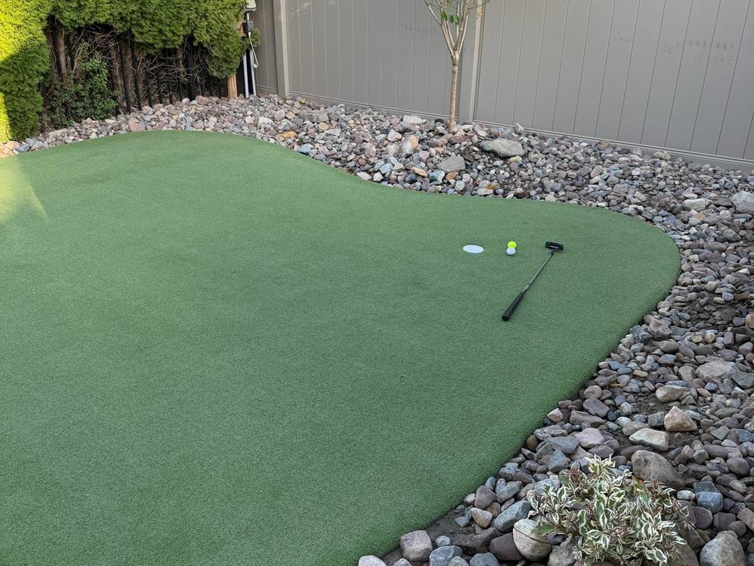 Artificial putting green bordered by rocks, golf balls, and a putter outdoors.