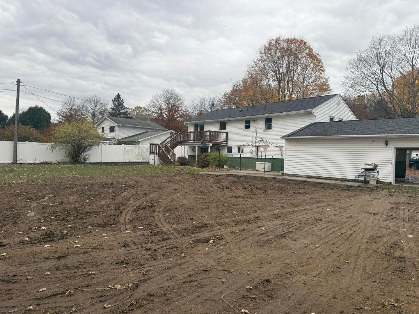 Dirt field in front of two-story white houses with detached garage, under a cloudy sky.