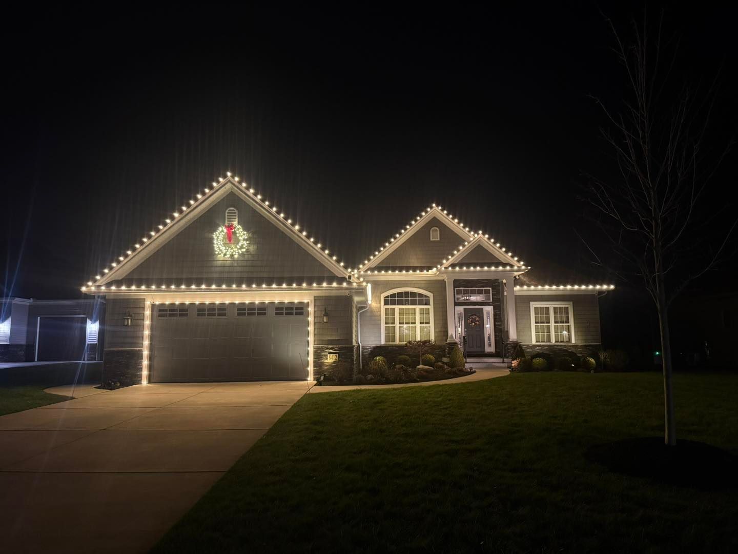 House at night with roofline Christmas lights and a wreath over the garage door.