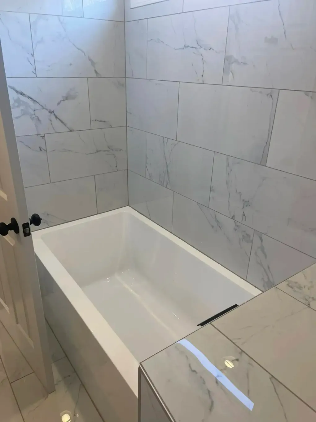White tiled bathroom with a built-in white bathtub and glass shower partition