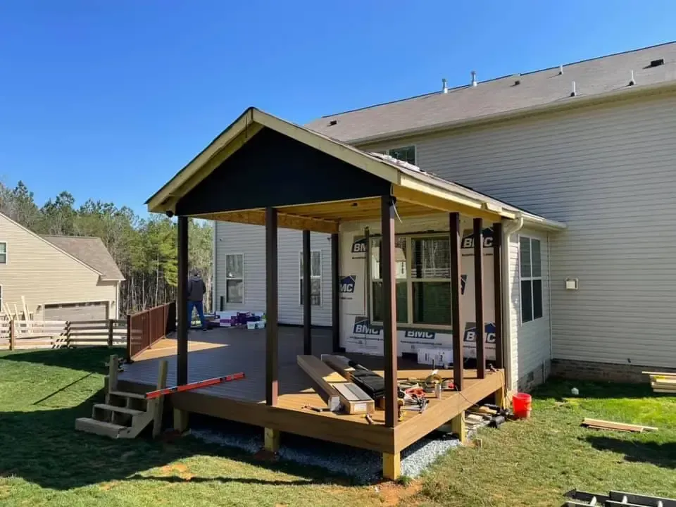 Covered wooden backyard deck with steps and black railings beside a house, under construction or renovation