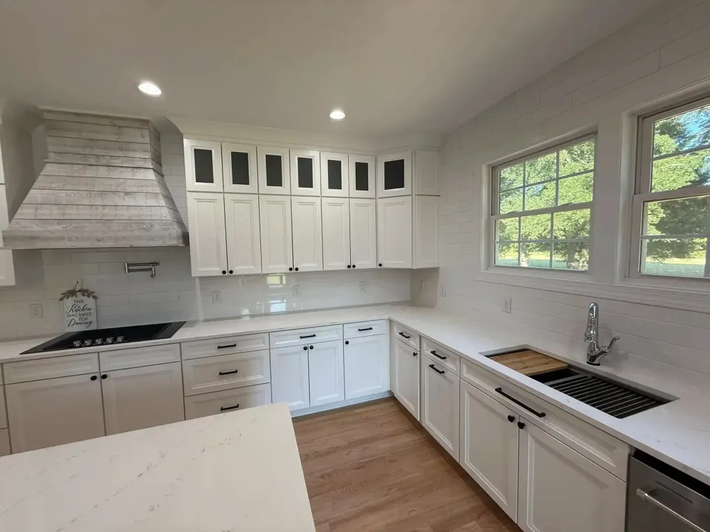 Bright white kitchen with cabinets, black countertops, farmhouse sink, and two large windows overlooking greenery