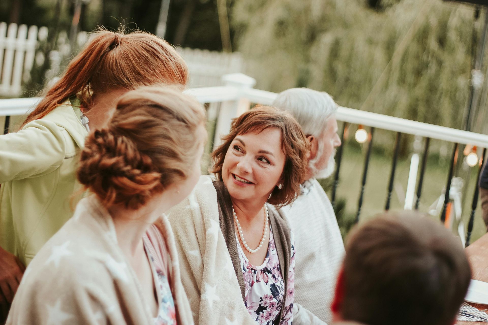 A group of people are sitting on a deck talking to each other.