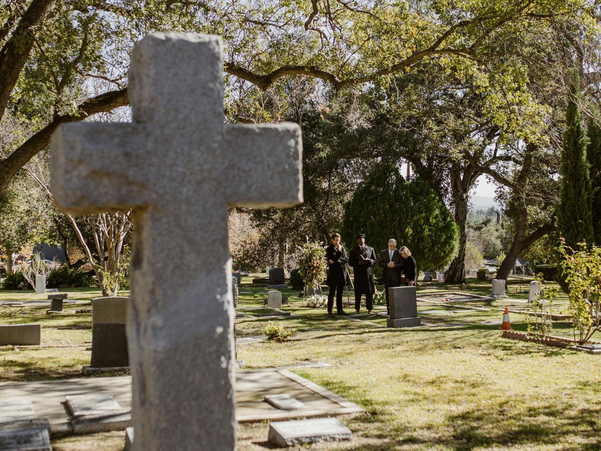 A group of people are standing in a cemetery with a cross in the foreground.