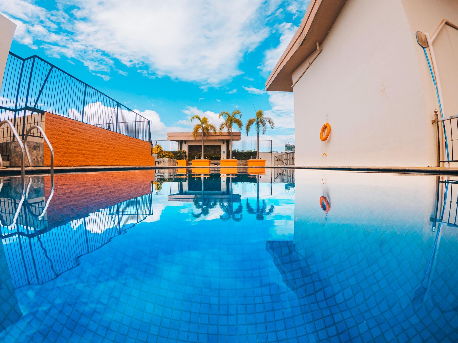 Infinity pool reflecting blue sky beside white buildings and orange loungers with palm trees in the background