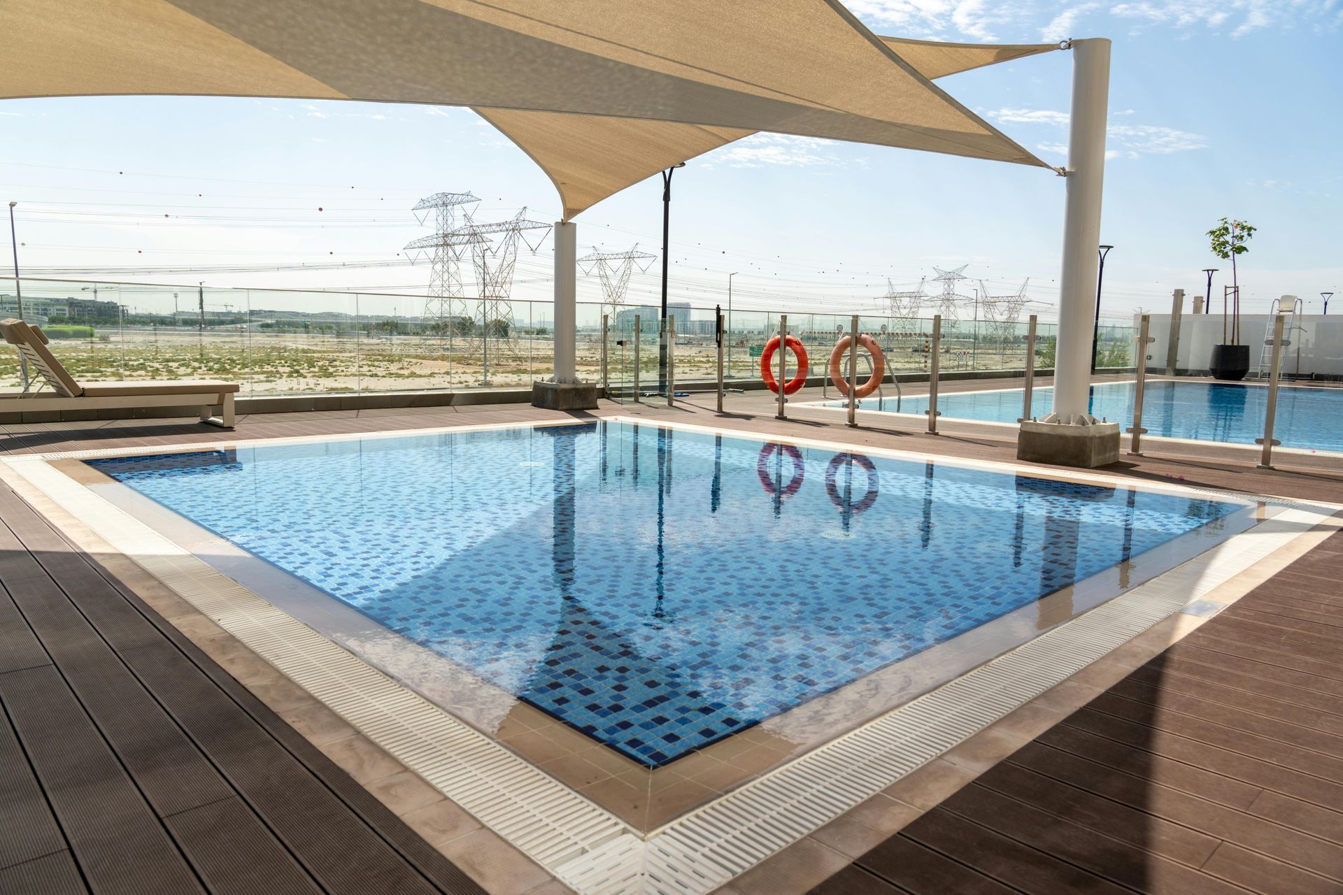 Rooftop pool with blue water, lounge chairs, and sunshade canopy overlooking the city skyline