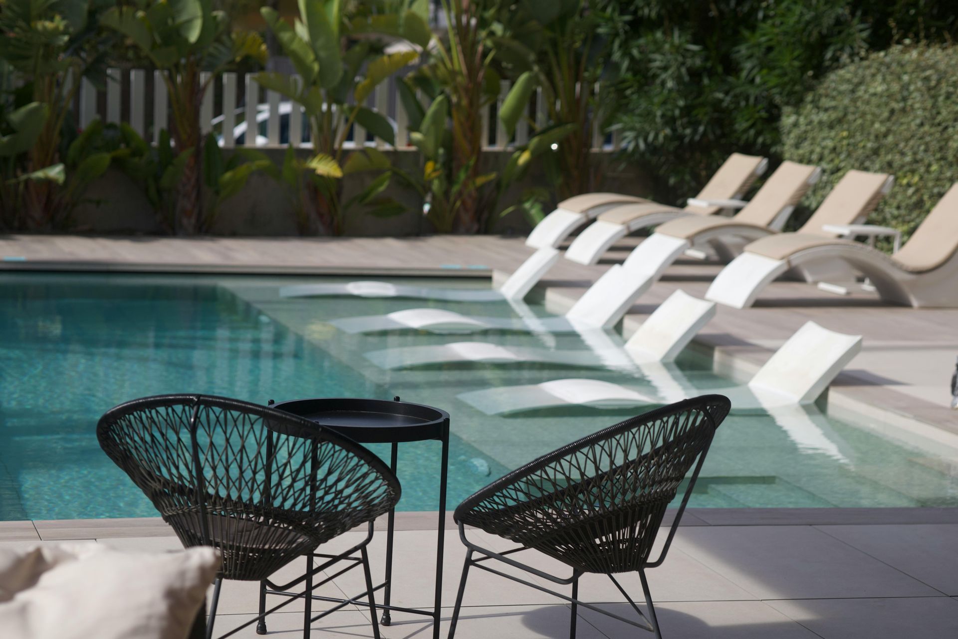 Poolside patio with black chairs and white lounge chairs beside a turquoise swimming pool.