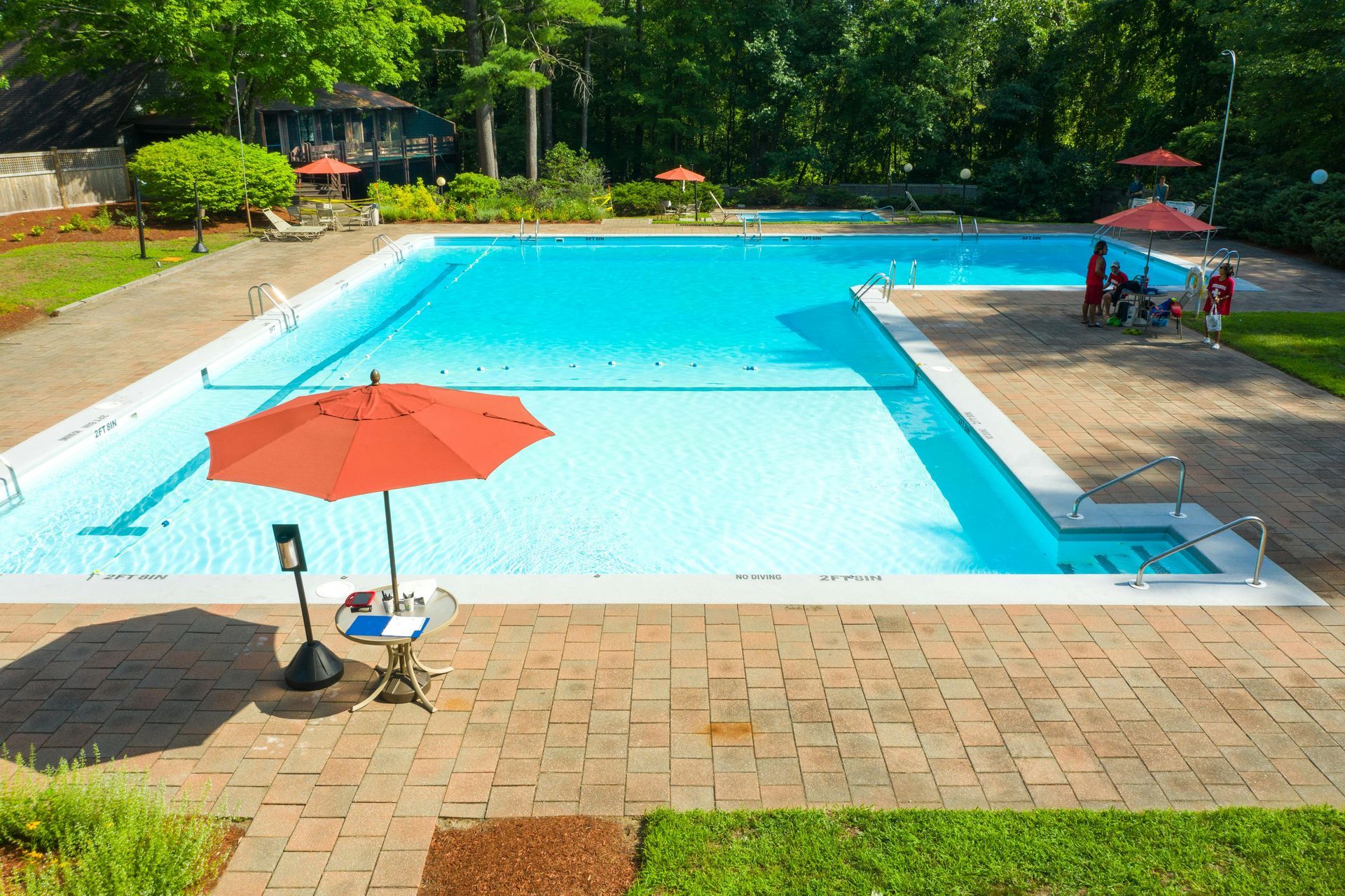 Outdoor swimming pool with bright blue water, orange umbrella, lounge chairs, and trees in the background
