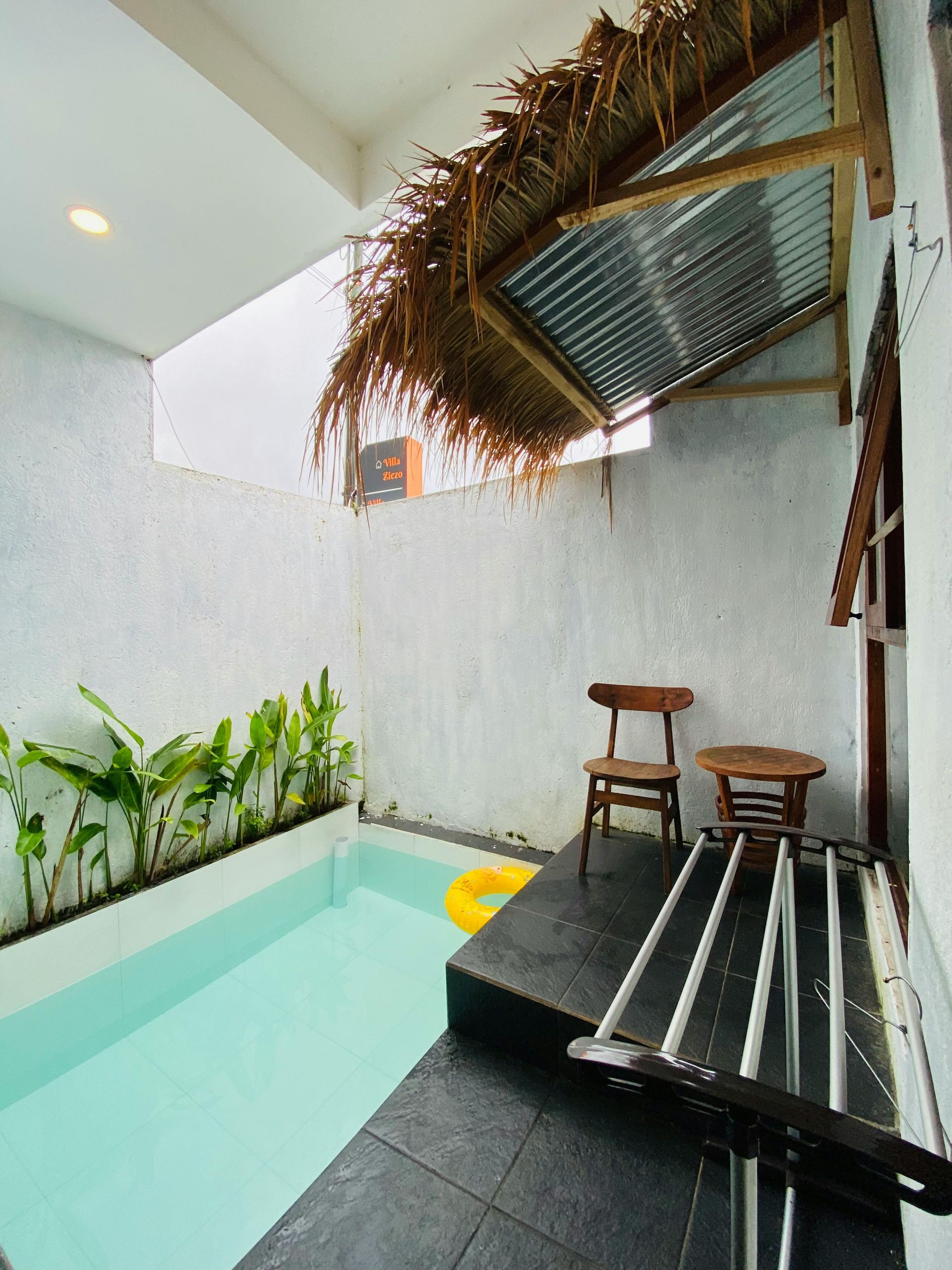 Small private pool patio with black deck, stools, and thatched canopy next to white walls