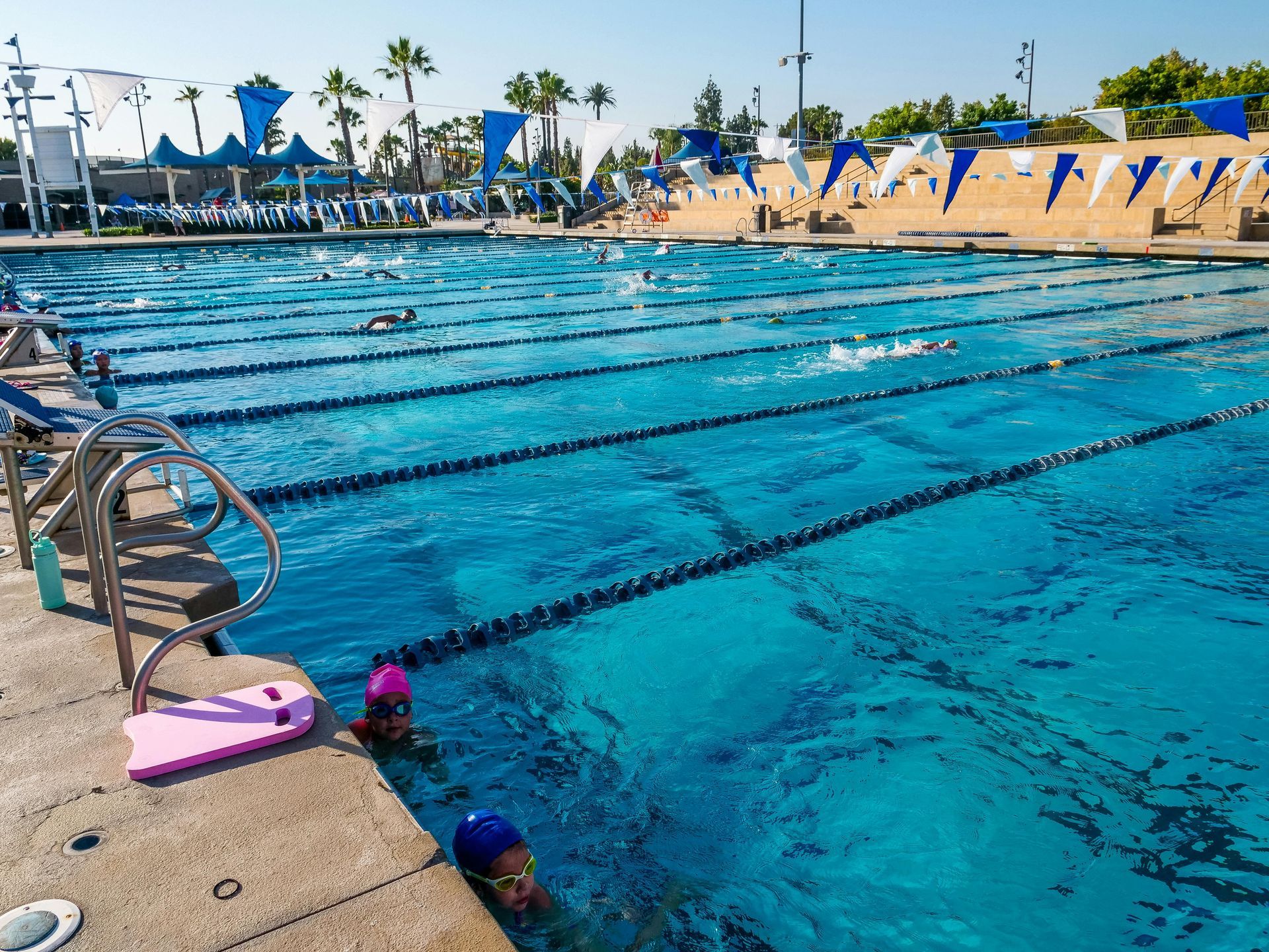 Outdoor lap pool with swimmers and blue lane markers on a sunny day