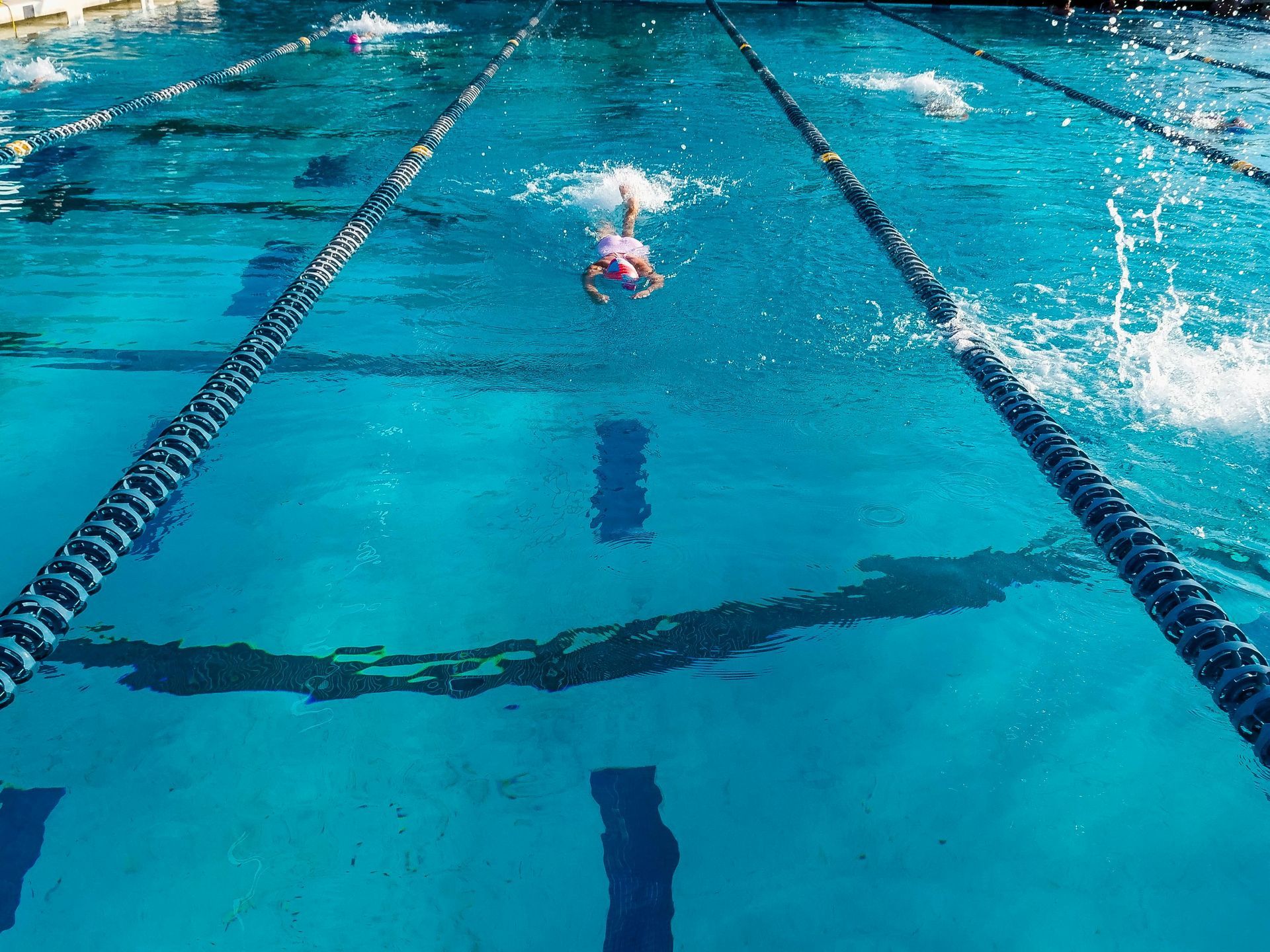Swimmer racing in a turquoise pool lane with splashing water