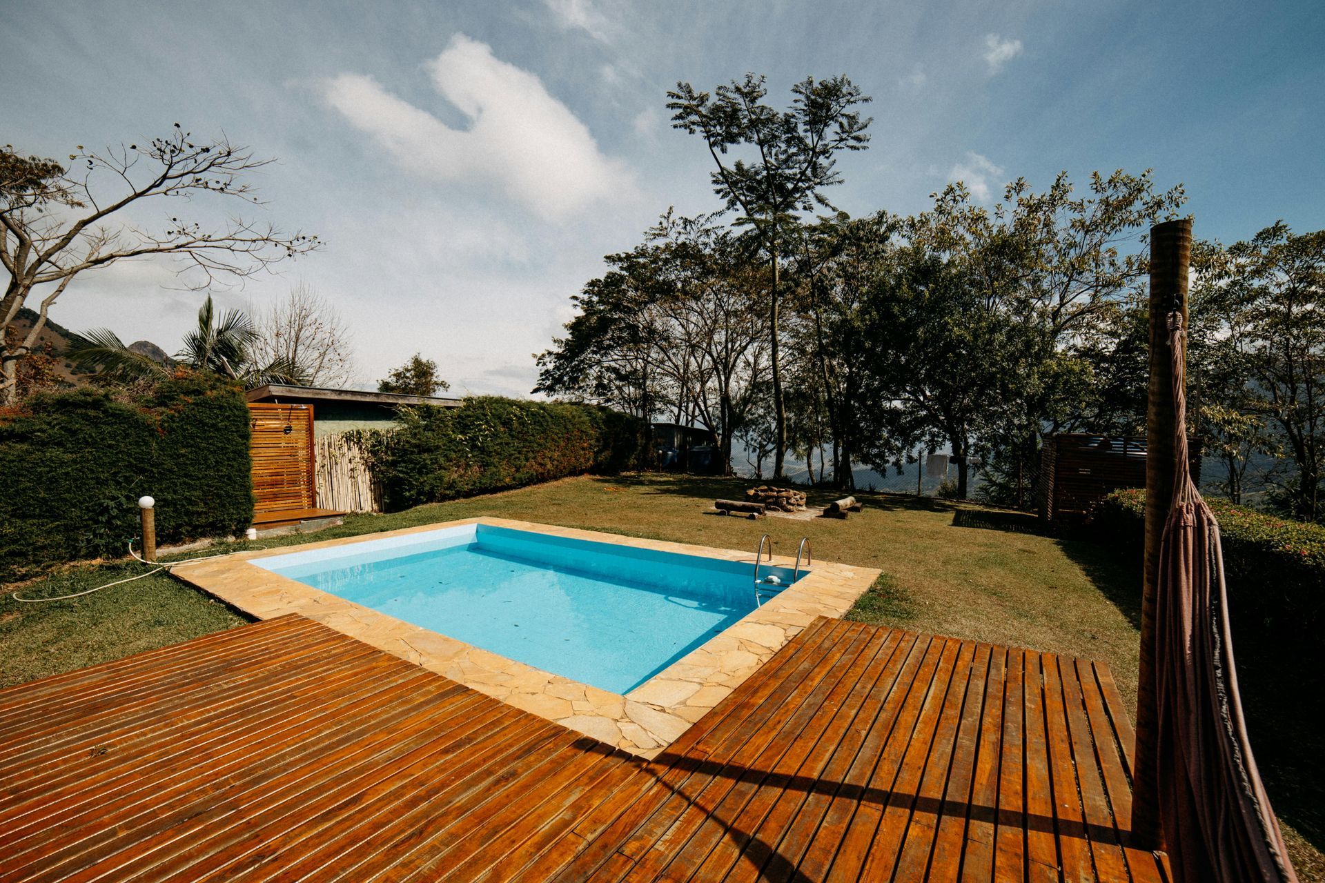 Backyard pool with wooden deck, trees, and a cloudy sky