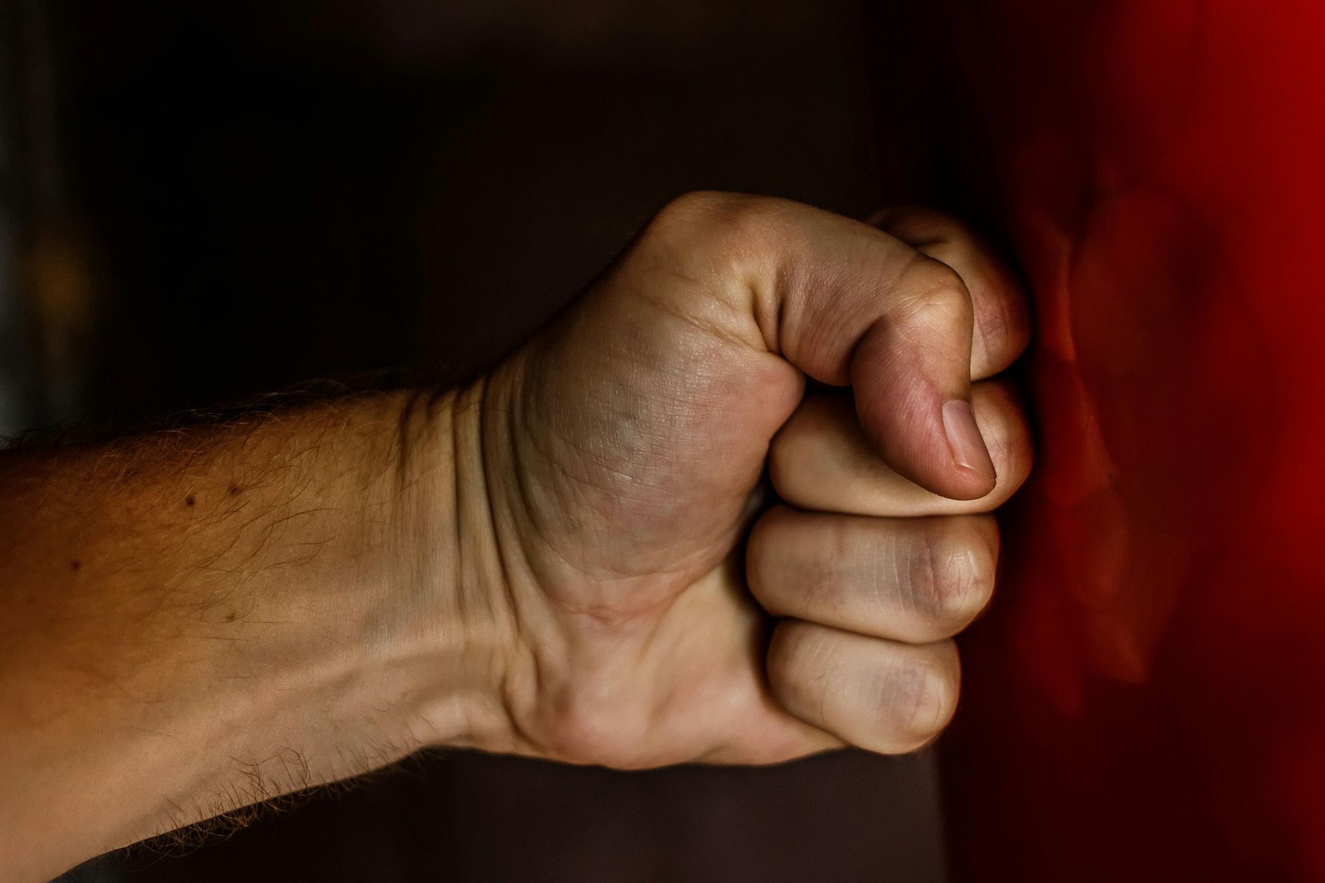 Hand clenching a fist against a red surface.