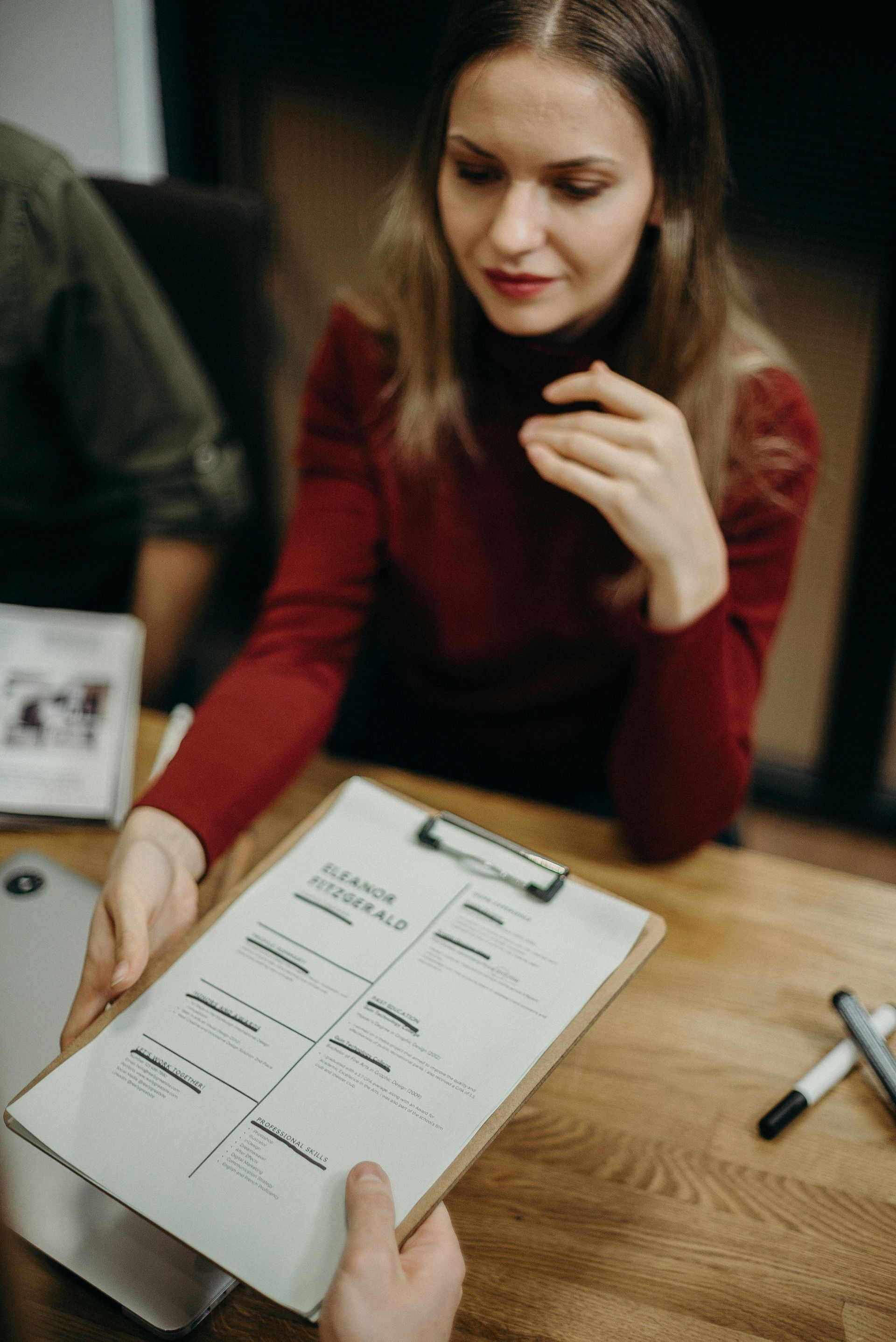 A woman is sitting at a table holding a clipboard.