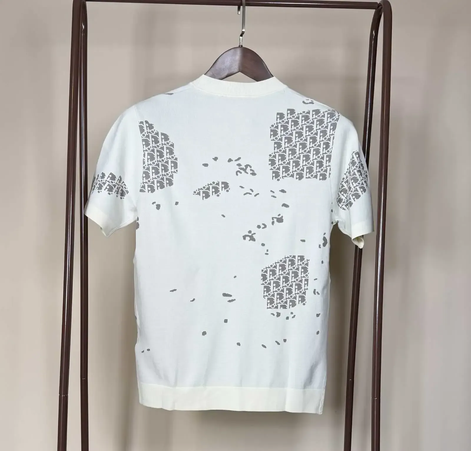 White knit t-shirt with gray logo pattern hanging on a wooden hanger on a brown rack.
