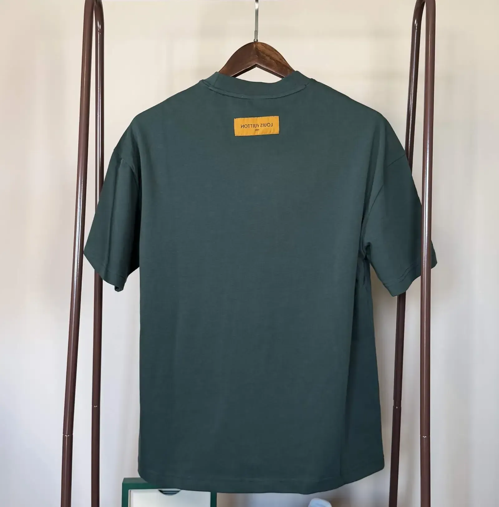 Green t-shirt with a white logo on a hanger, displayed on a clothing rack.