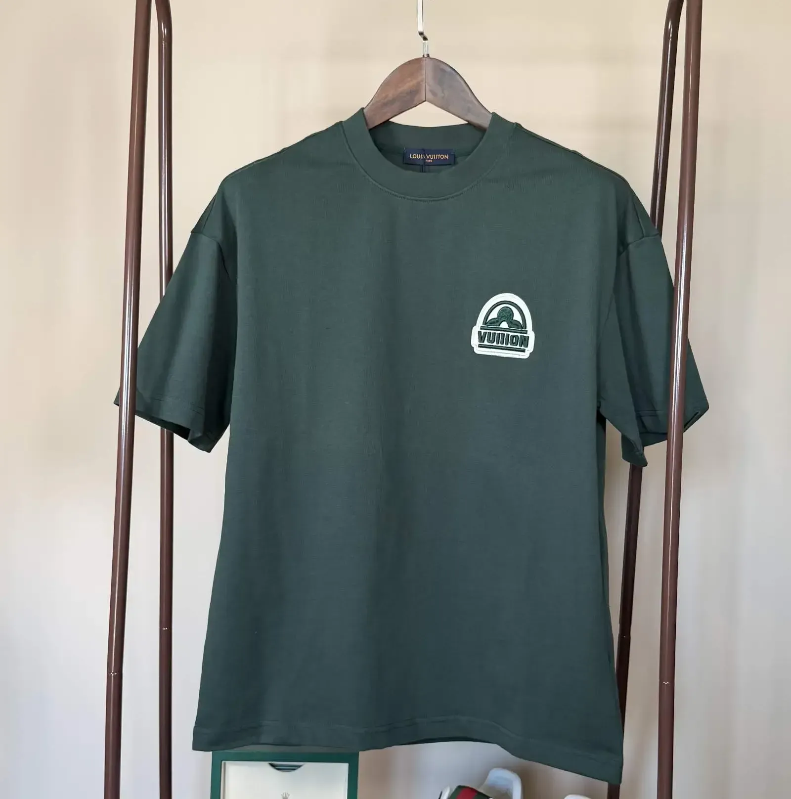 Green t-shirt with a white logo on a hanger, displayed on a clothing rack.