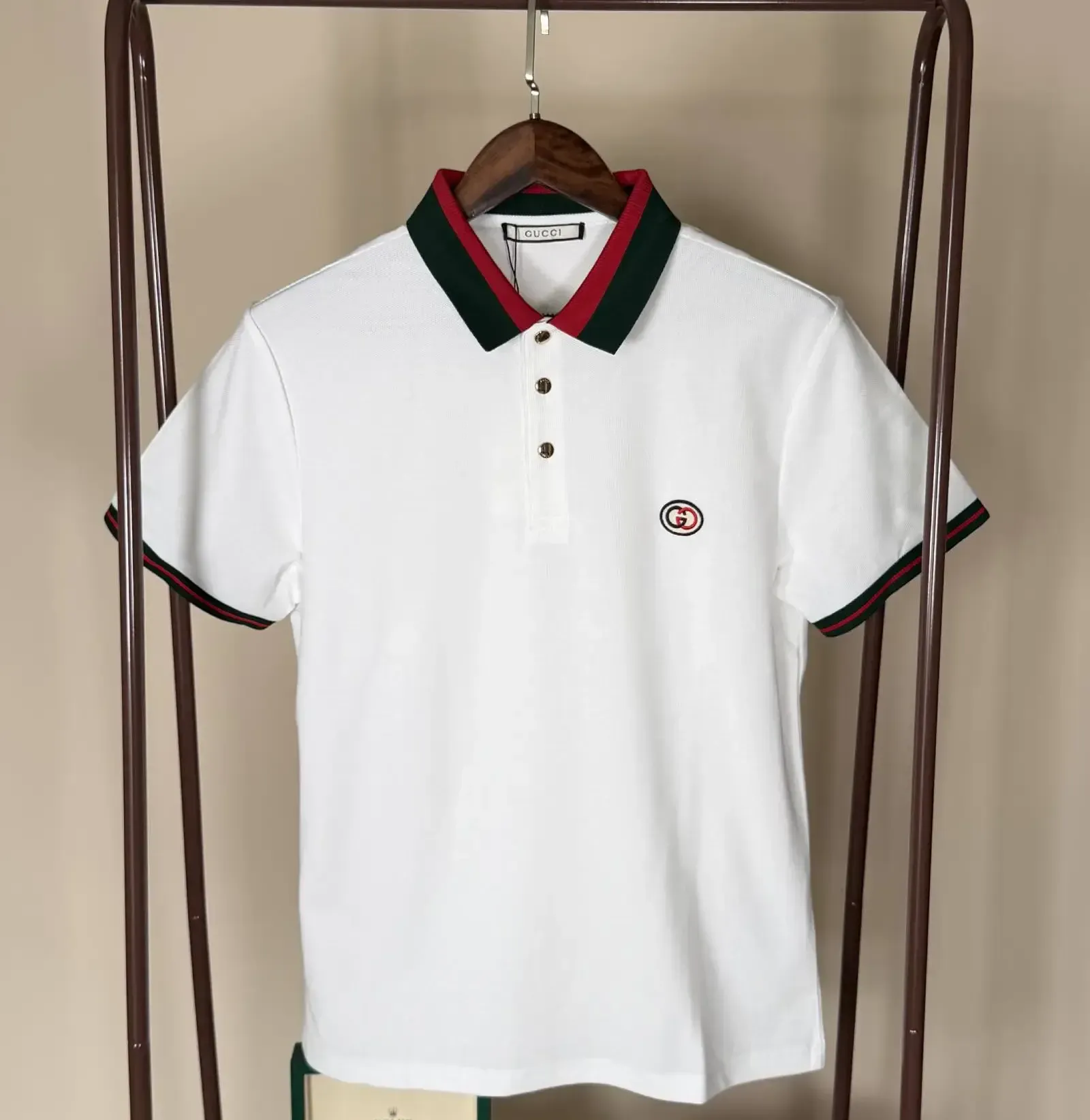 White polo shirt with green and red collar trim, Gcci logo, hanging on a rack.
